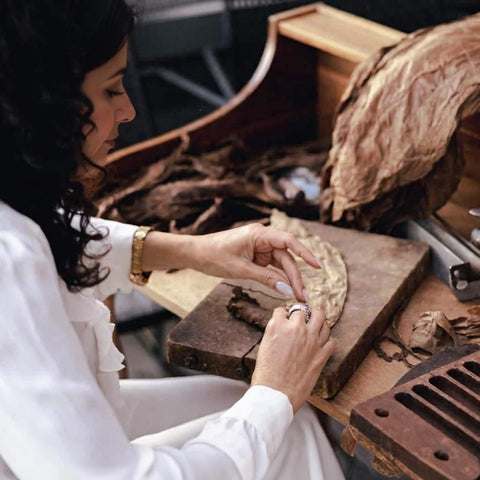 Woman working with cigar leaf on a wooden board in a rustic setting