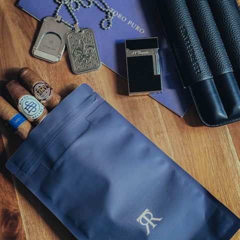 Cigars, a lighter, and a blue pouch on a wooden surface with 'R' logo.