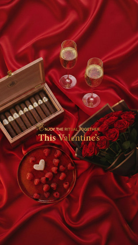 Valentine's Day arrangement with chocolates, cigars  roses, and champagne on red fabric.