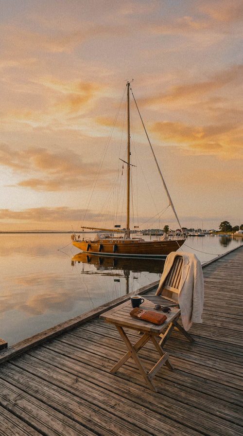 Leather Toro Puro cigar case and one coffee on a jetty table at sunrise, sailing boat moored behind.