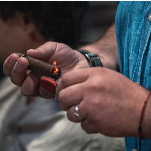 Person lighting a cigar with a lighter, wearing a blue shirt.