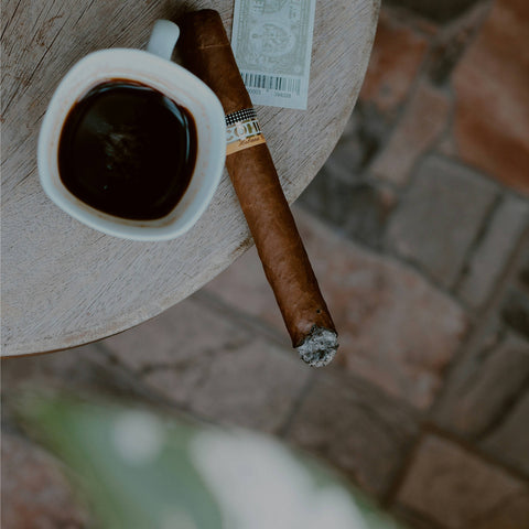 Cigar and cup of coffee on a wooden table with a blurred outdoor background
