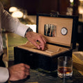 Rapport Brompton large humidor open at a bar, a hand selecting a cigar beside a glass of whisky - Toro Puro